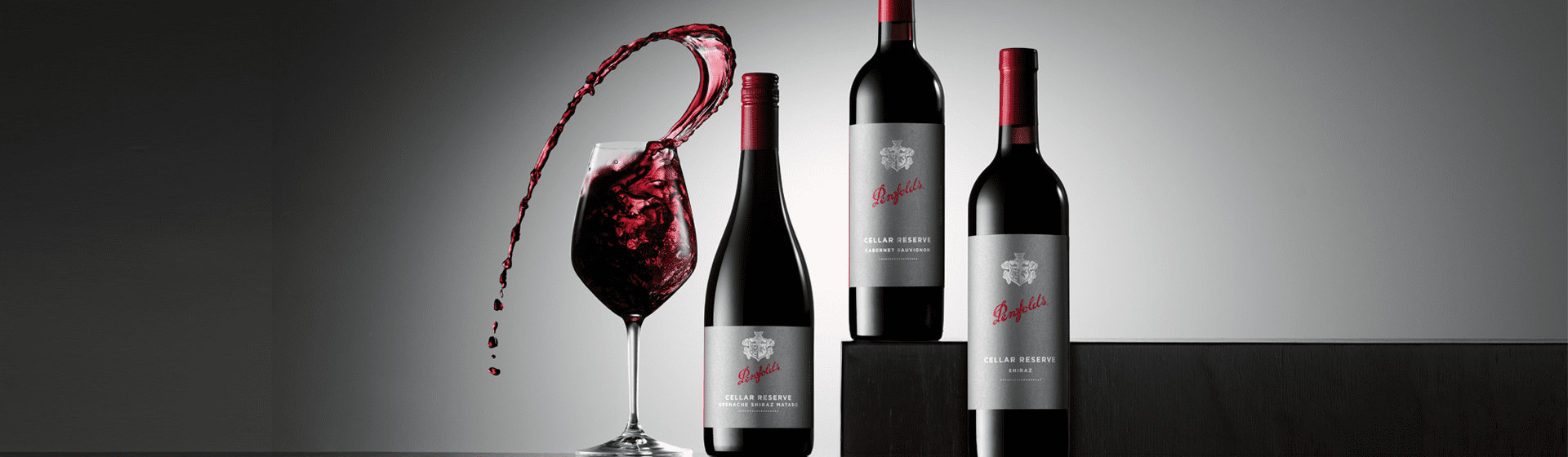 Three Cellar Reserve bottles with dark labels.  Wine glass with dramatic liquid mid air sits beside